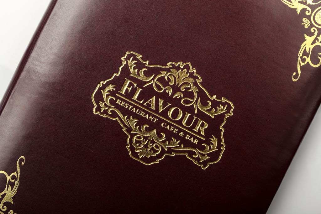 Flavour Restaurant menu cover — burgundy leather, gold logo embossing and ornament, close-up