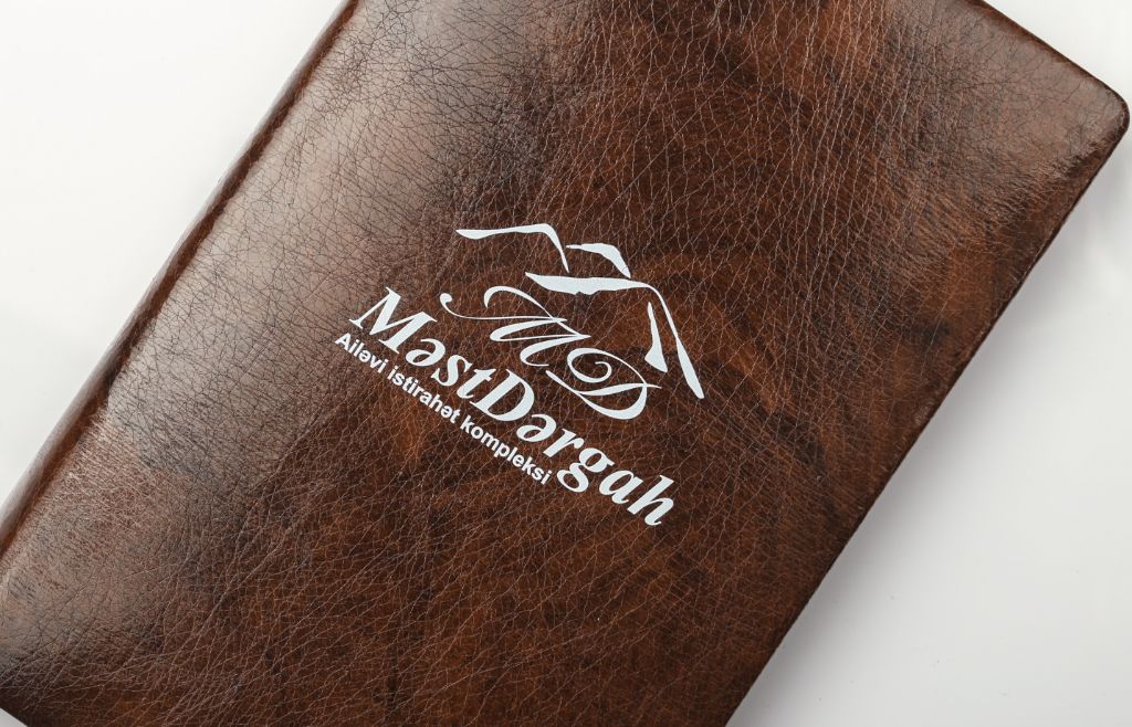 MəstDərgah menu cover — brown vintage leather, silver logo, close-up