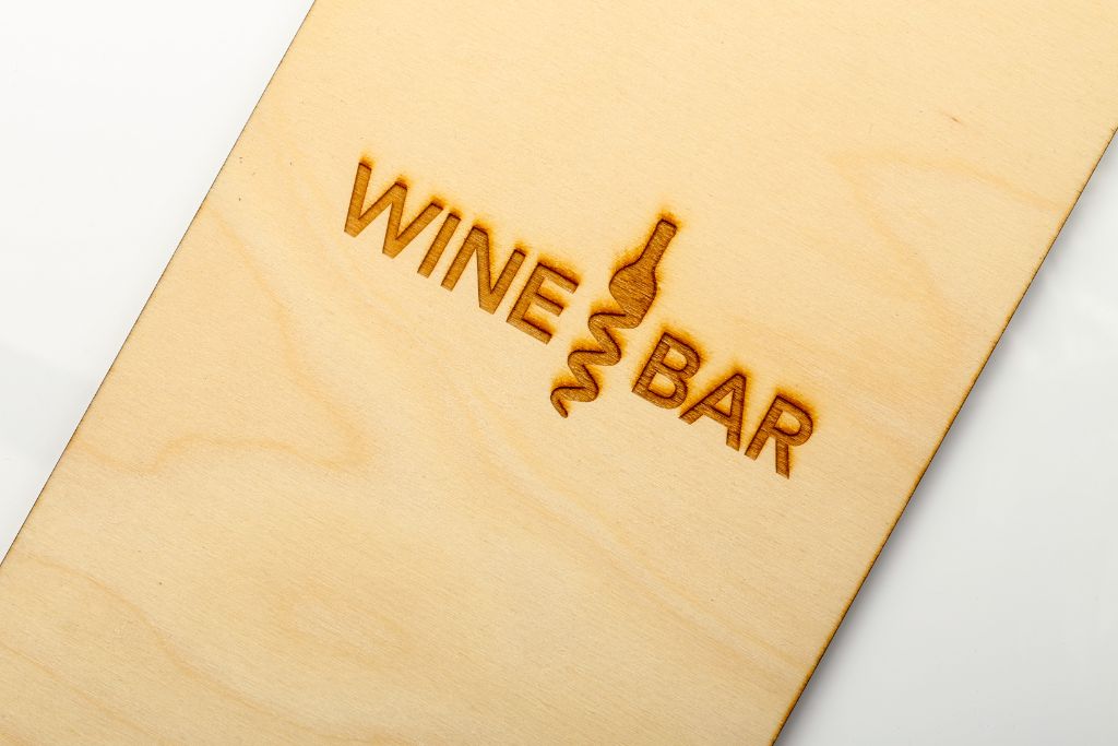 Wine Bar menu cover — light wood, laser logo engraving, close-up