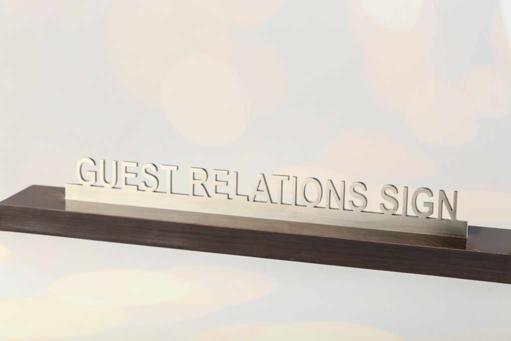 3D cut metal letters GUEST RELATIONS SIGN — stainless steel, matte brushed finish, wenge wood base, side view