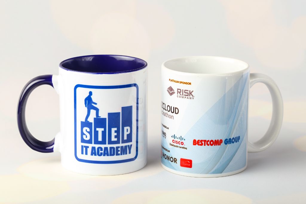 Branded mugs STEP IT Academy and AzCloud Hackathon — white with blue handle and inner part, sublimation print, front view