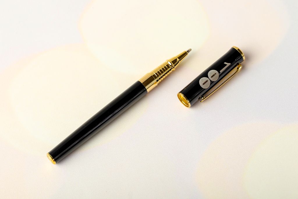 Black metal rollerball pen with gold details — cap removed, logo on cap