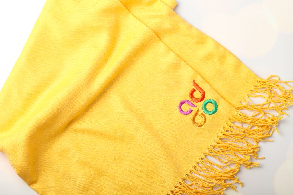 ADGO scarf — yellow cashmere, fringe corner, close-up of logo embroidery