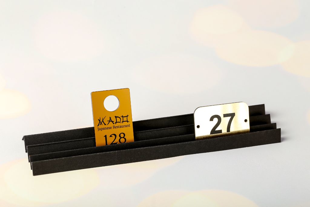 Room number tags for MADO restaurant — gold anodised aluminium, number 128, hanging style